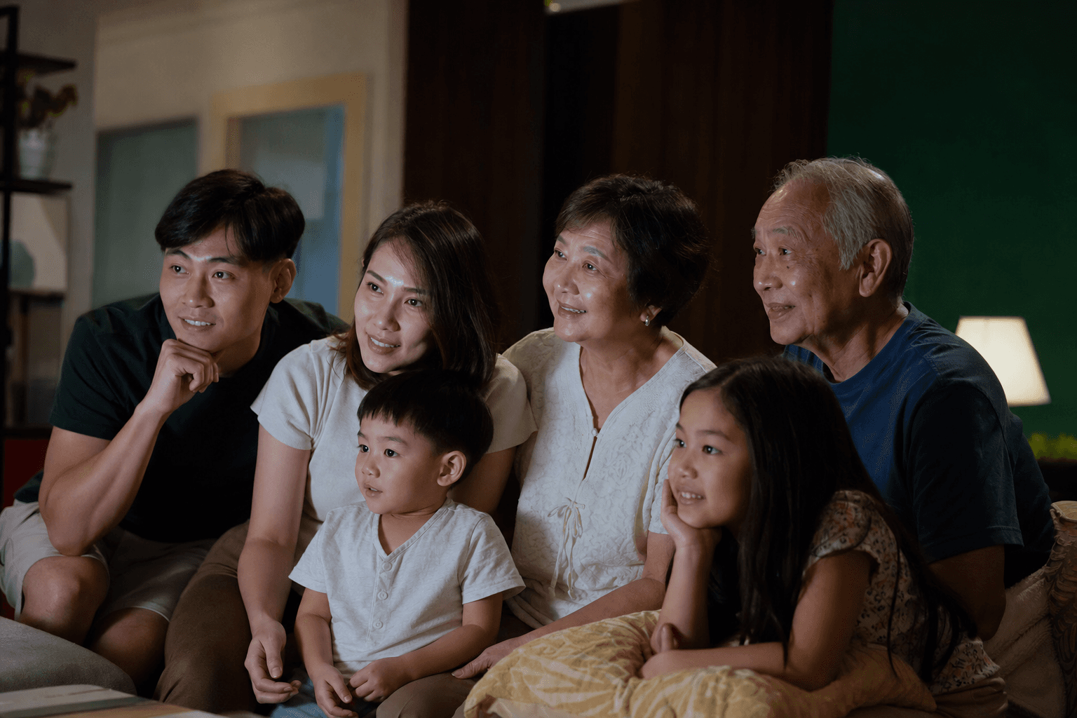 Multigenerational family sitting together on a sofa watching a screen with warm attentive expressions